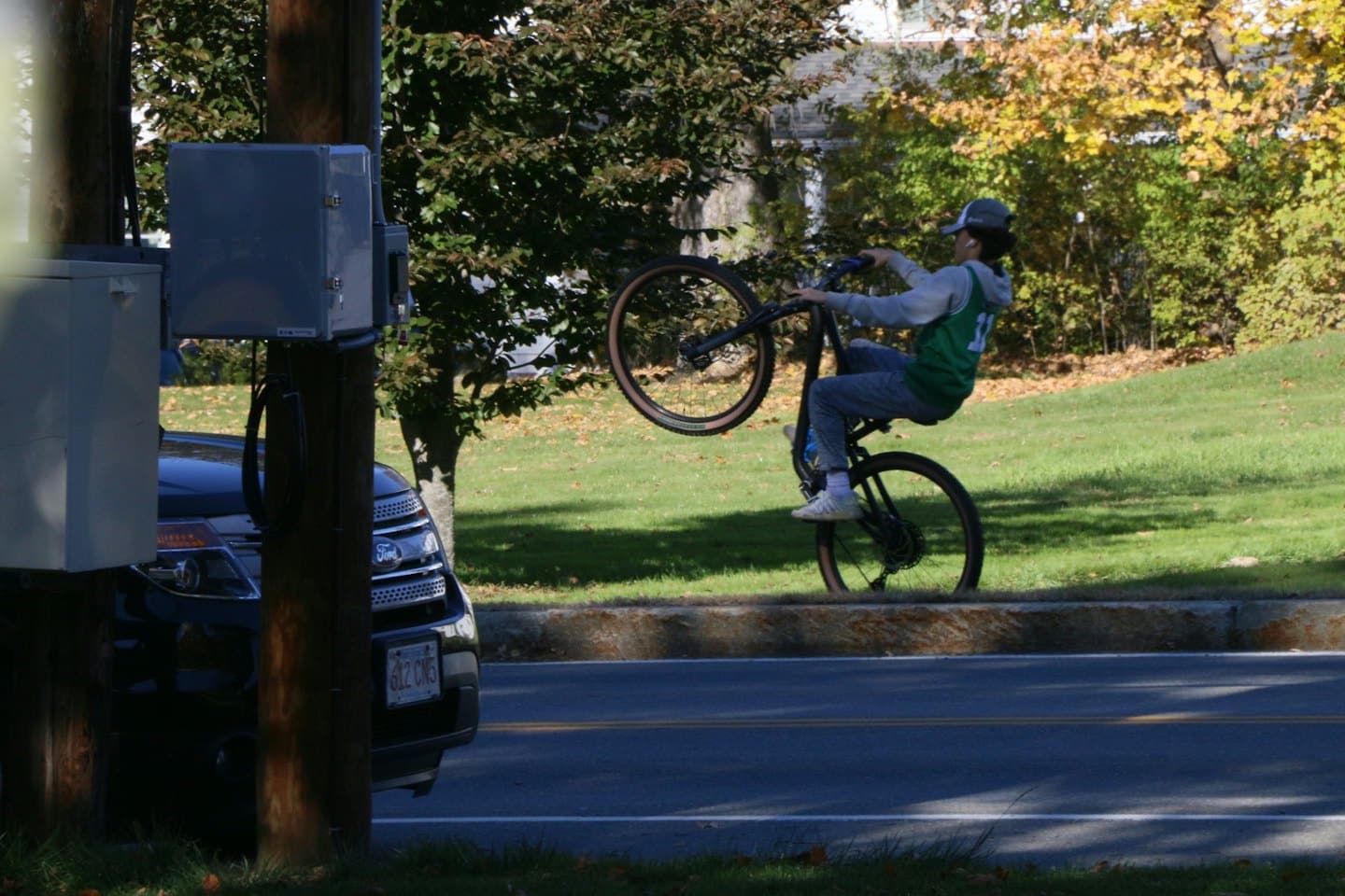A cyclist performs a wheelie on a paved road.