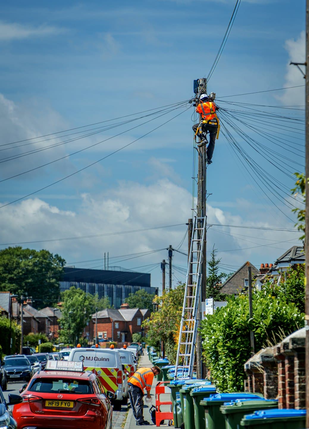 Utility technicians working on a residential street with overhead wires.