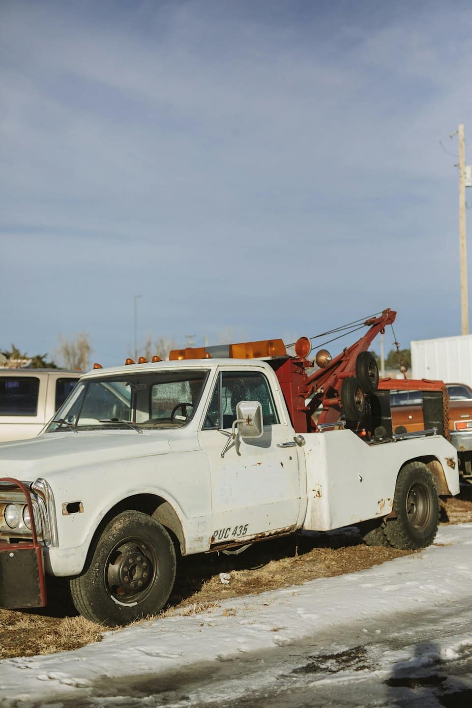 Vintage white tow truck with orange light bar on snowy grass.