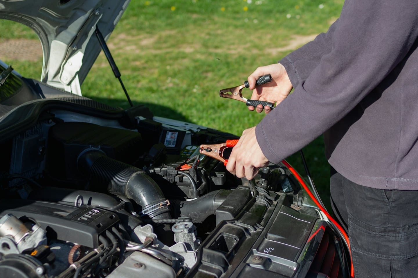 Hands connect jumper cables to a car battery.