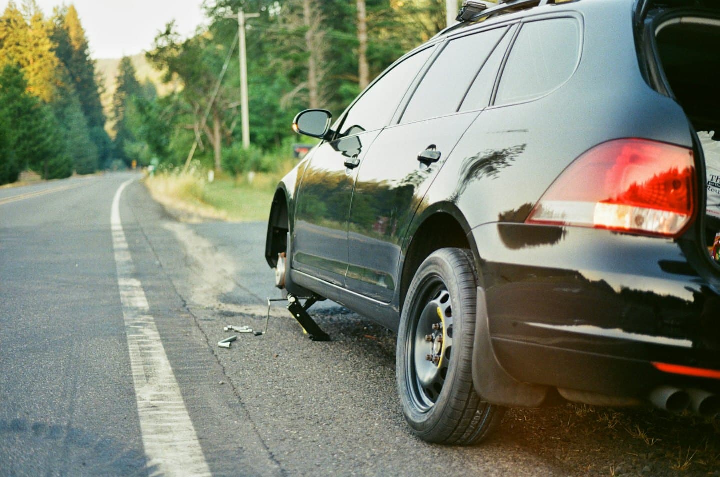 Black station wagon on roadside changing a flat tire.