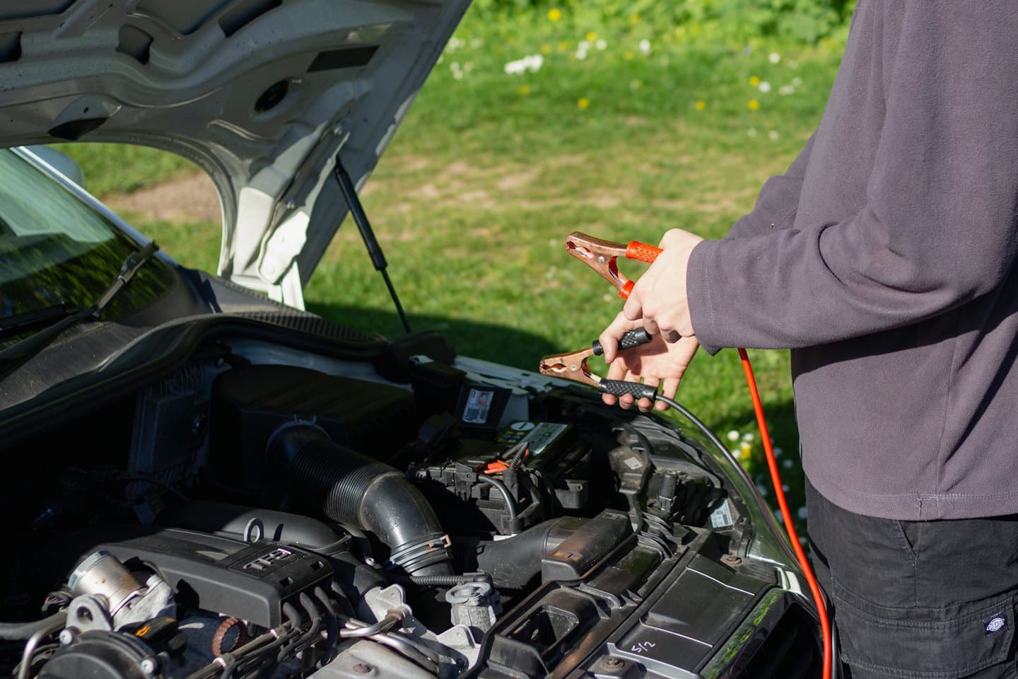 Hands holding jumper cables over a car engine.